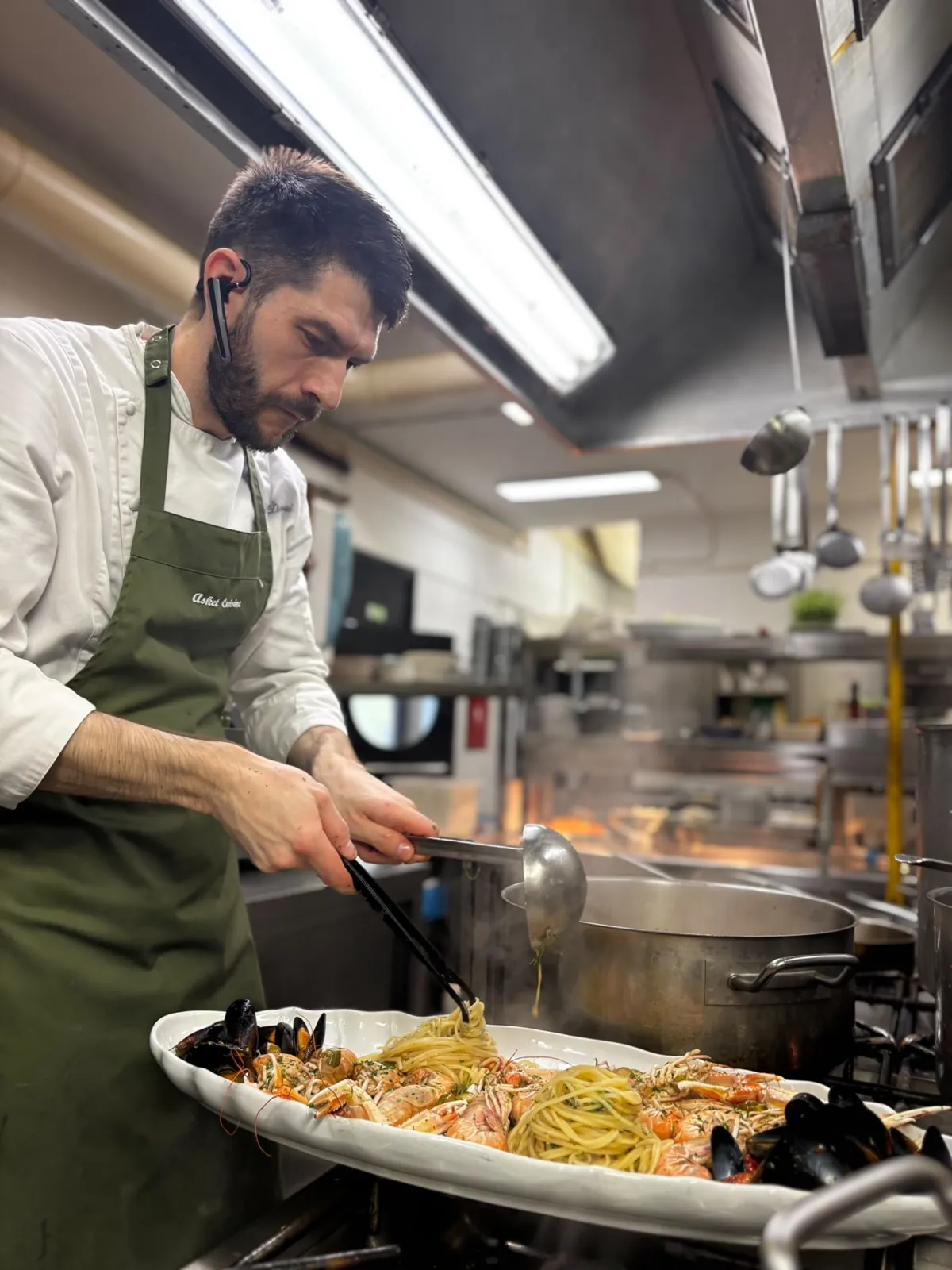 Nenad Živković plating seafood spaghetti in the kitchen, Asket Cuisine apron